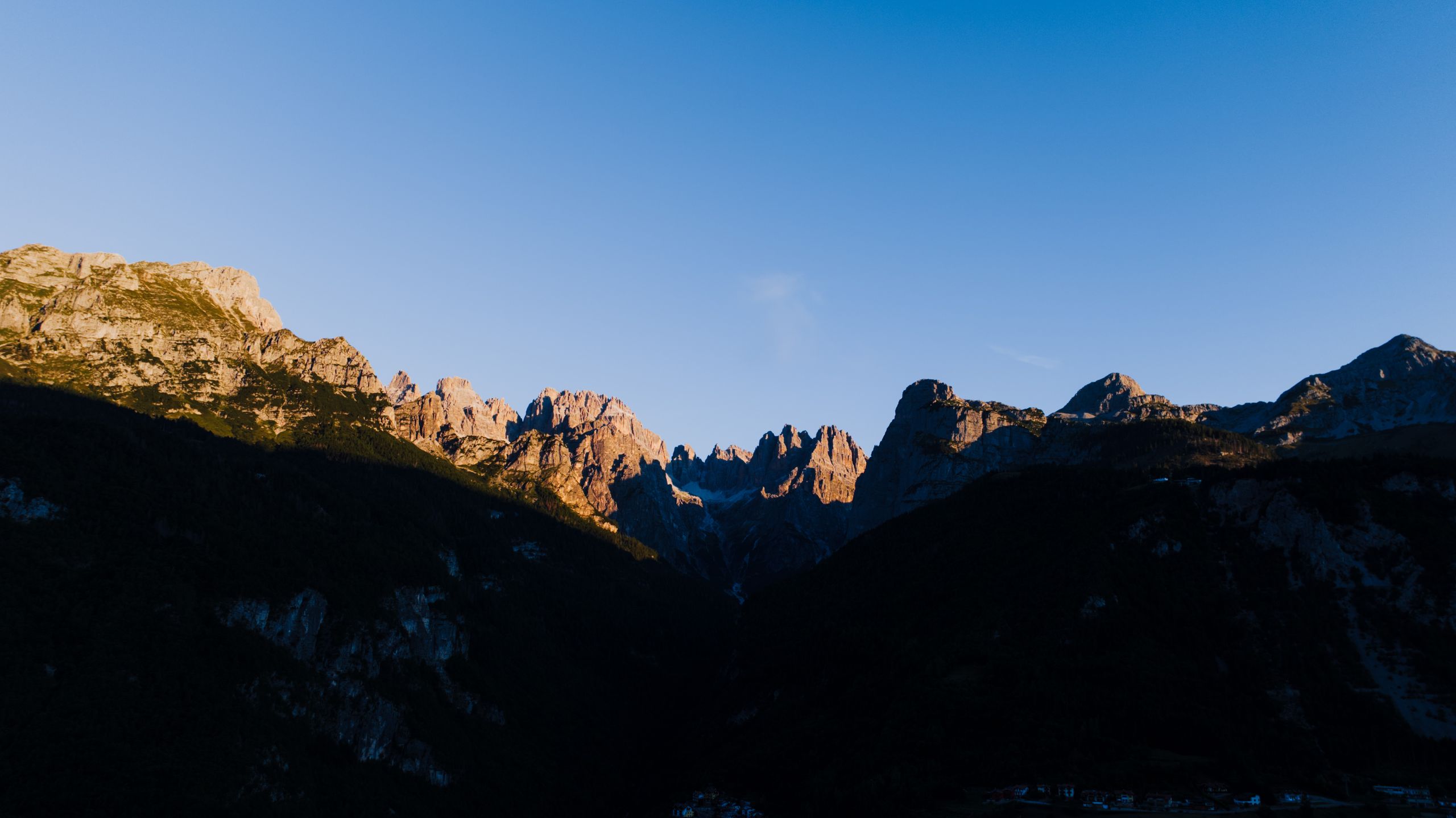 La primera luz del sol ilumina las cumbres de los Dolomitas bajo un cielo azul